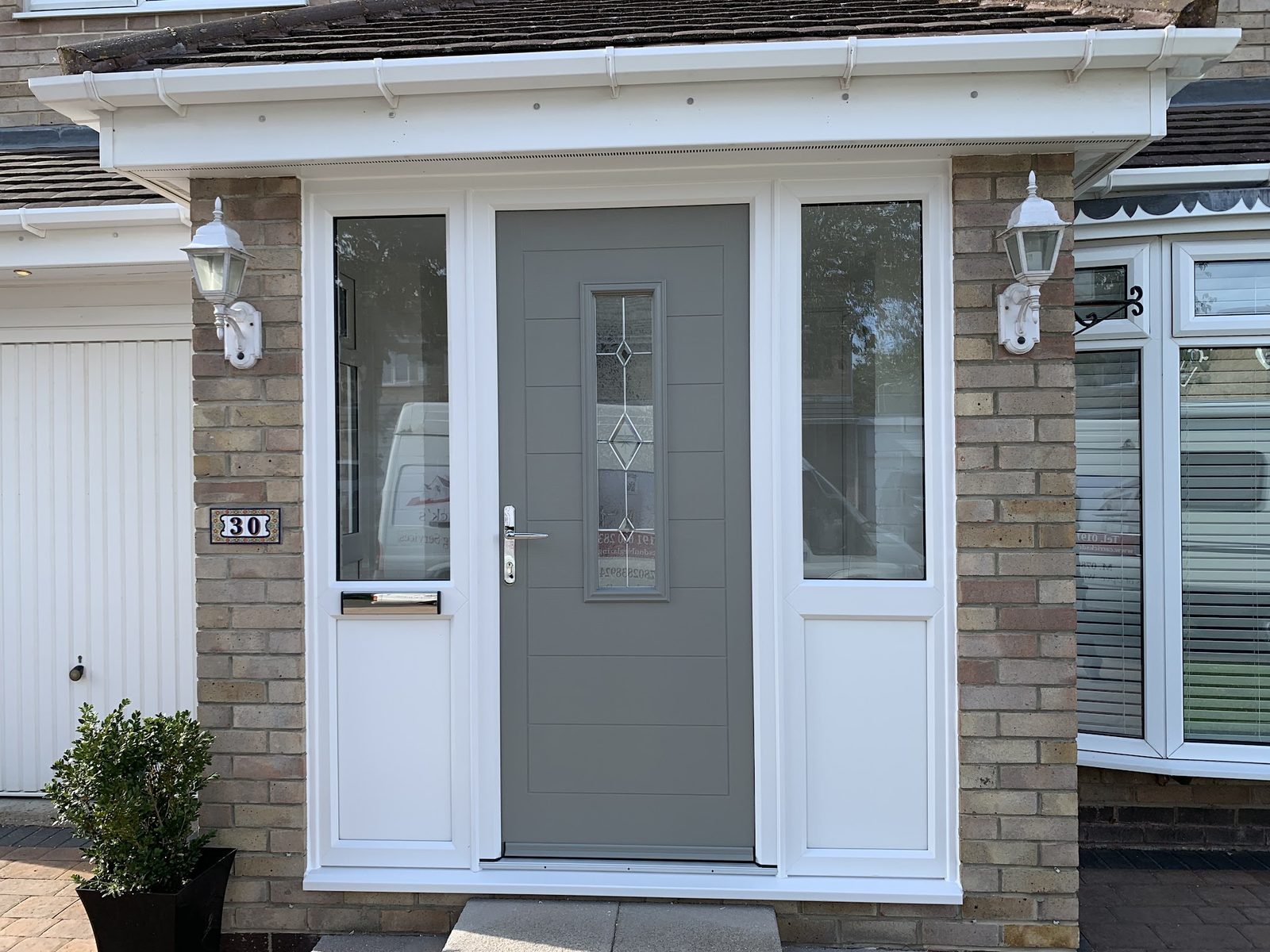A grey composite front door in a white-framed porch with wall lights either side
