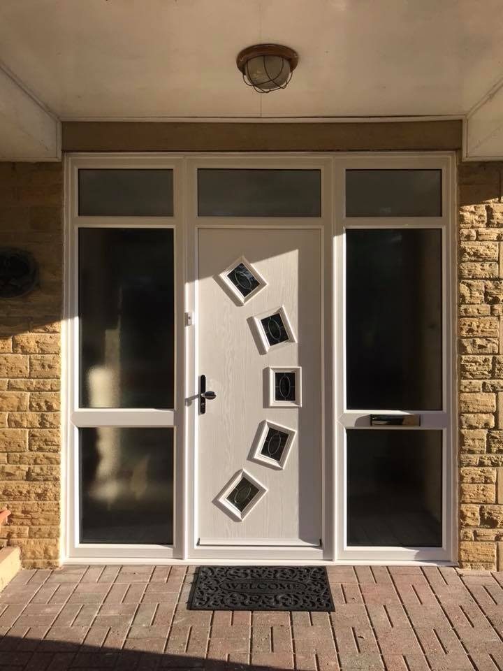 A pale composite door with diamond glazing under a brick-pillared canopy