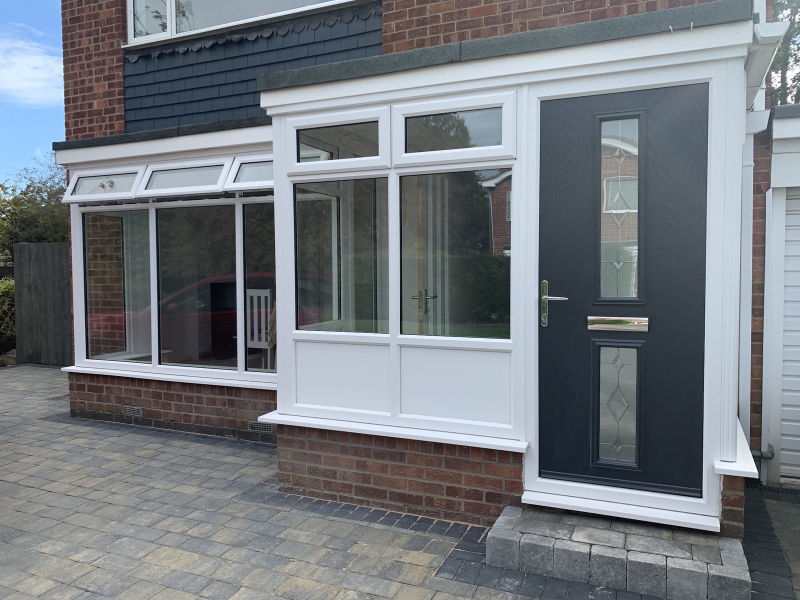 An anthracite front door in a white porch, with a bay window beside it